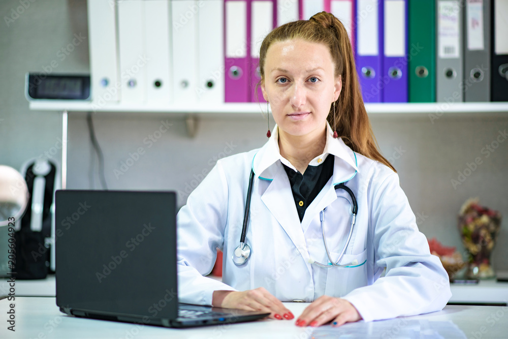Portrait of female doctor sitting in office with laptop in white coat