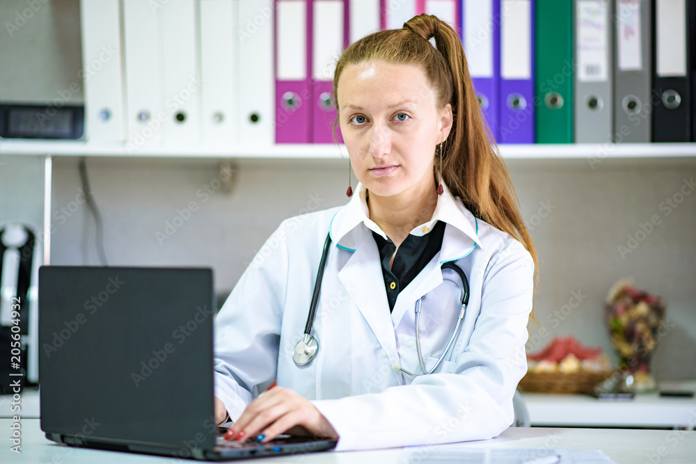 Portrait of female doctor sitting in office with laptop in white coat Portrait of female doctor sitting in office with laptop in white coat