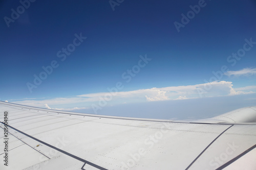 Part of airplane wing and clouds in blue sky was photographed on the plane.