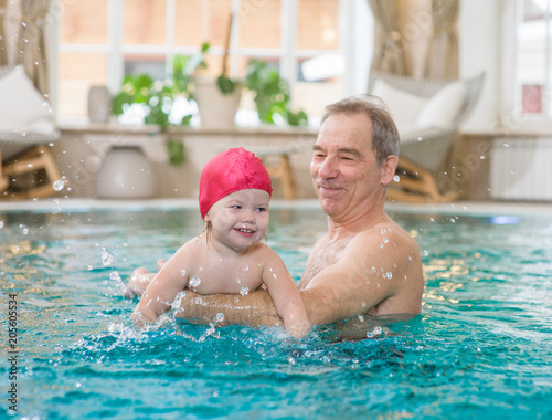 grandfather teaches a little girl to swim in the pool