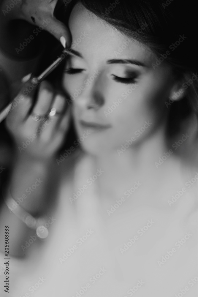 Naklejka premium beautiful stylish bride with red hair getting make up done by professional stylist, morning preparation. wedding getting ready, space for text. expert beauty artist. black white photo