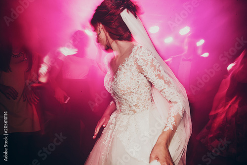 stylish happy bride dancing at wedding reception. gorgeous wedding couple having fun and partying in restaurant in light show. newlywed emotional moment. space for text