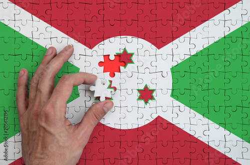 Burundi flag  is depicted on a puzzle, which the man's hand completes to fold photo