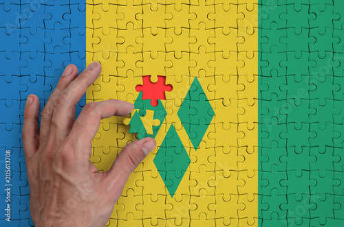 Saint Vincent and the Grenadines flag  is depicted on a puzzle, which the man's hand completes to fold photo