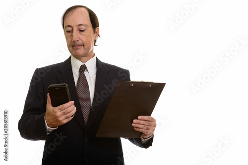 Studio shot of mature businessman using mobile phone while holdi