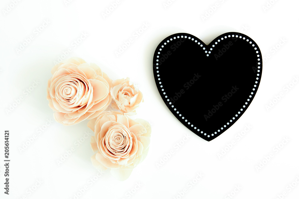 Black love heart with three artificial flowers beside it on a white surface Black love heart with three artificial flowers beside it on a white surface