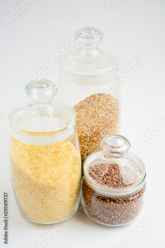 three transparent containers with a grain of rice, buckwheat and lentils on a light background