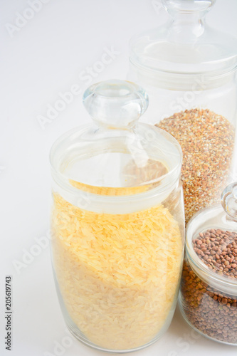 three transparent containers with a grain of rice, buckwheat and lentils on a light background