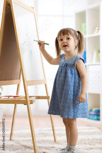 Child girl drawing on a white board with a felt-tip pen. photo