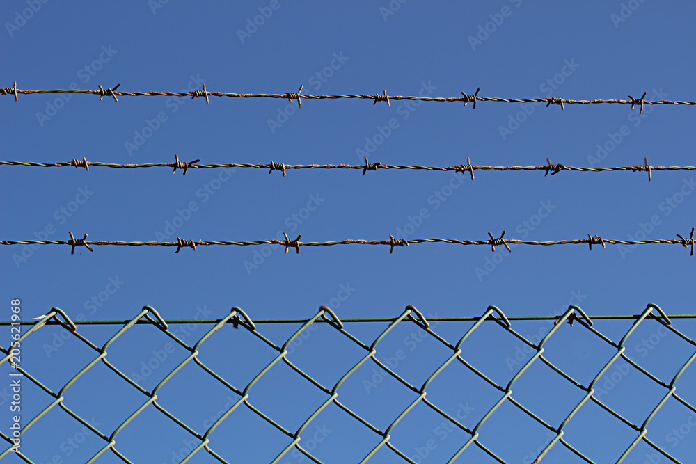 A barbed metal wire and fence against the blue sky 1 A barbed metal wire and fence against the blue sky 1