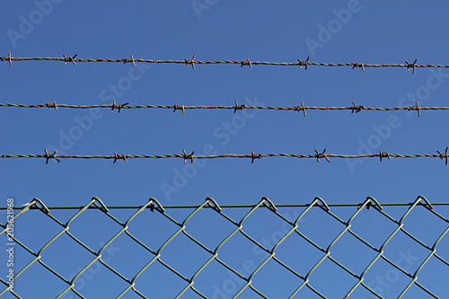 A barbed metal wire and fence against the blue sky 1