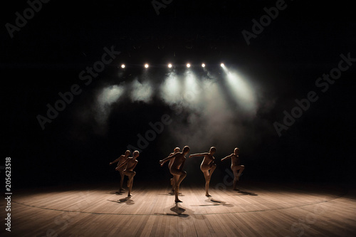 A group of small ballet dancers rehearses on stage with light and smoke