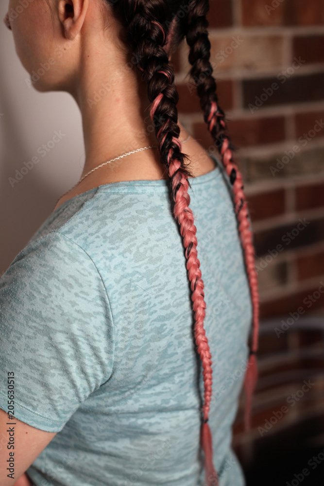 Girl with two braids natural color dirty pink, brown, fashionable youth hairstyle with kanekalon, close-up of the girl's back, thin pigtails