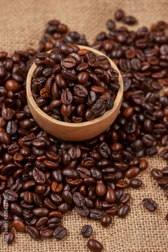 Wooden bowl with roasted coffee beans on rustic background.