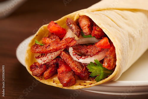 Shawarma with meat, tomato, onions and parsley on dark table