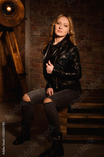 sexy blonde woman in leather clothes posing against wooden studio wall