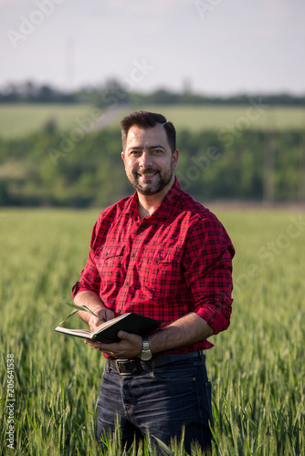 Young handsome farmer with diary standing in wheat field