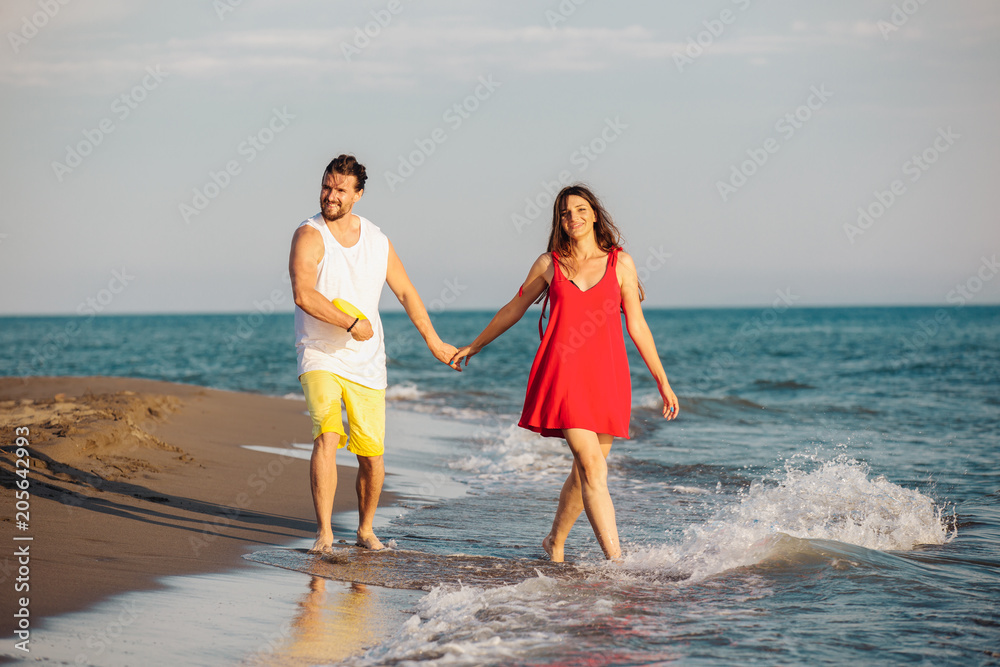 Young happy smiling couple holding hands walking on beach