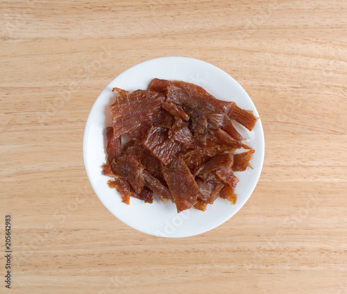 Pieces of turkey jerky on white plate atop a wood table.