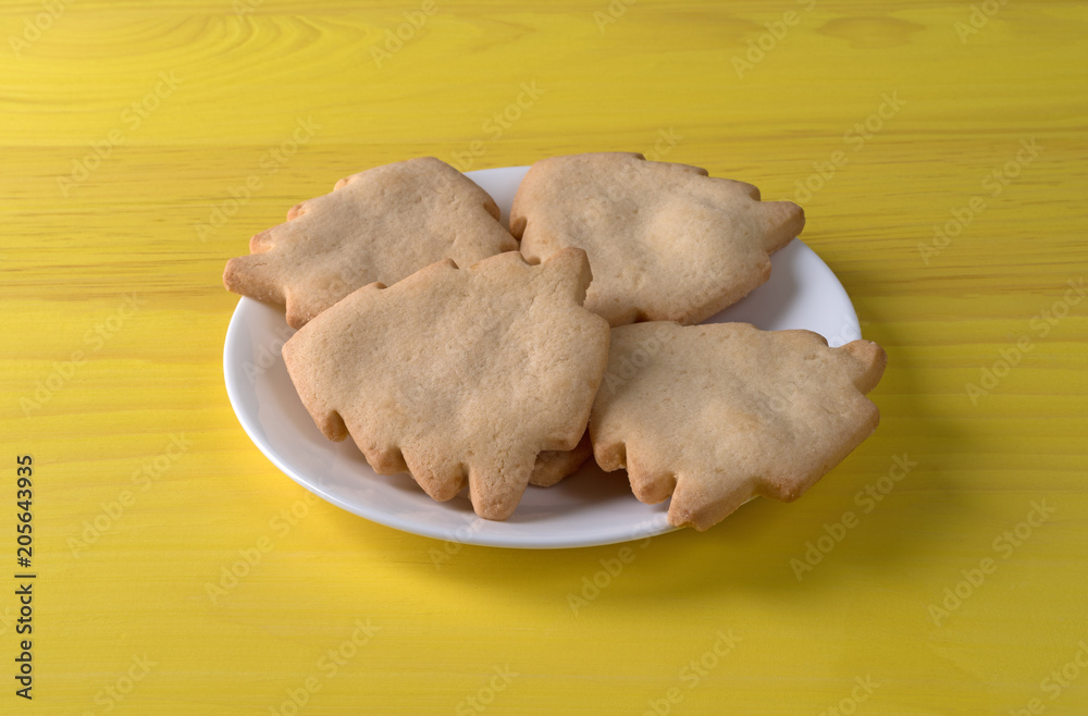 Fototapeta premium Tree shaped Christmas cookies on a white plate atop a yellow table.