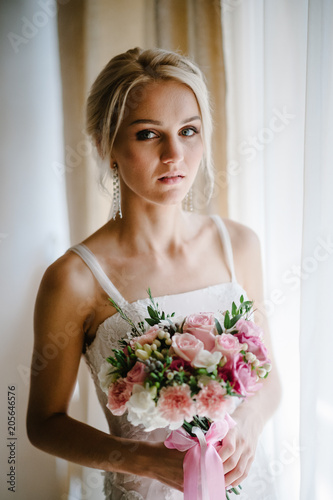 Serious portrait of bride with luxury make-up and hairstyle with a wedding bouquet of flowers, standing in studio indoor photo.