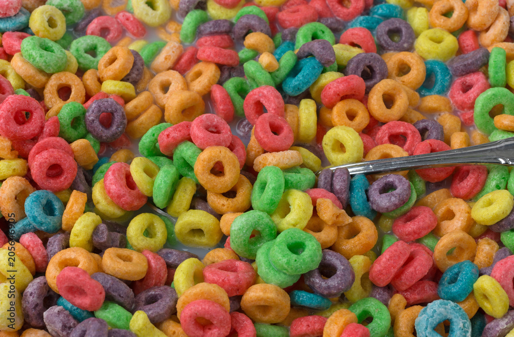 Close view of sugar coated fruity flavored cereal with milk and a spoon.