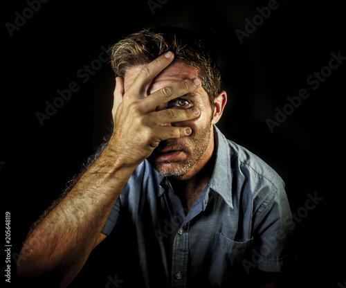 dramatic portrait of young attractive man covering face with hands but opening fingers to see and spy with one eye in curious and worried face expression