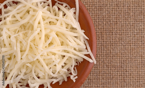 Top close view of sharp white cheddar cheese in a small bowl on a brown tablecloth.