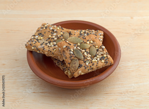 Whole wheat seeded crackers in a small bowl on a wood table.