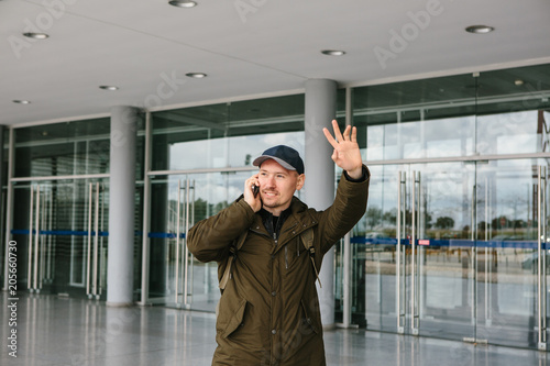 A young male tourist at the airport or near a shopping center or station calls a taxi or talks on a cell phone or communicates with friends using a mobile phone photo