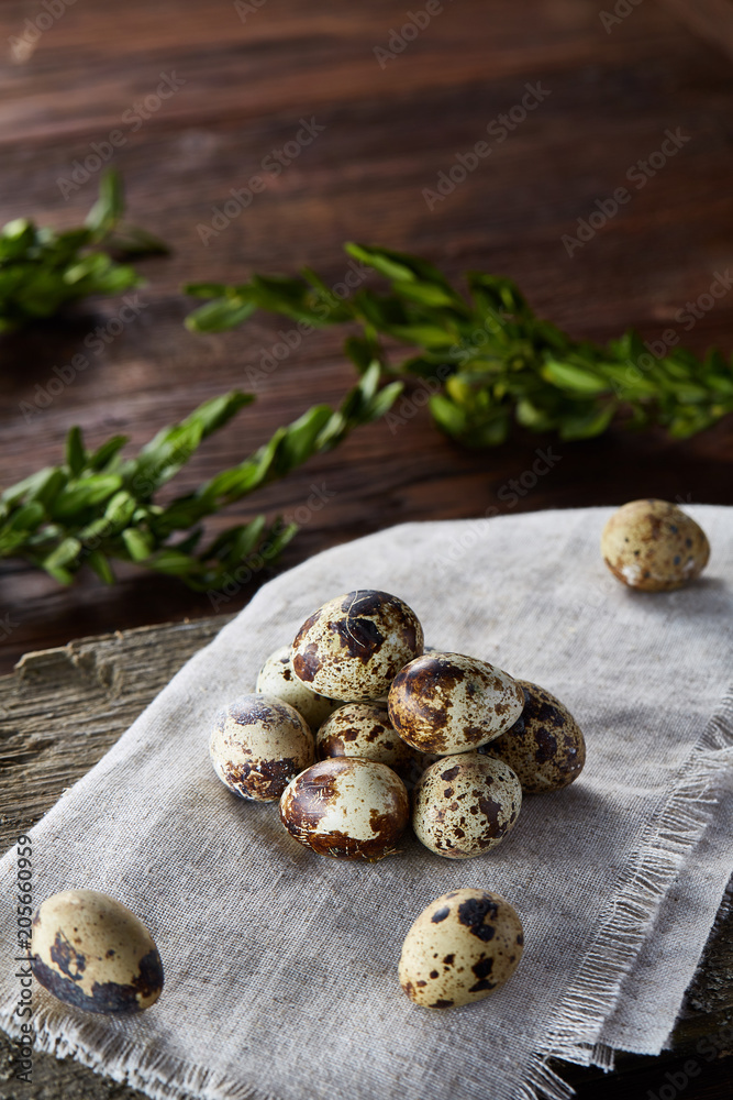 Quail eggs arranged in pyramid on a napkin with boxwood branches over a wooden table, close-up, selective focus.