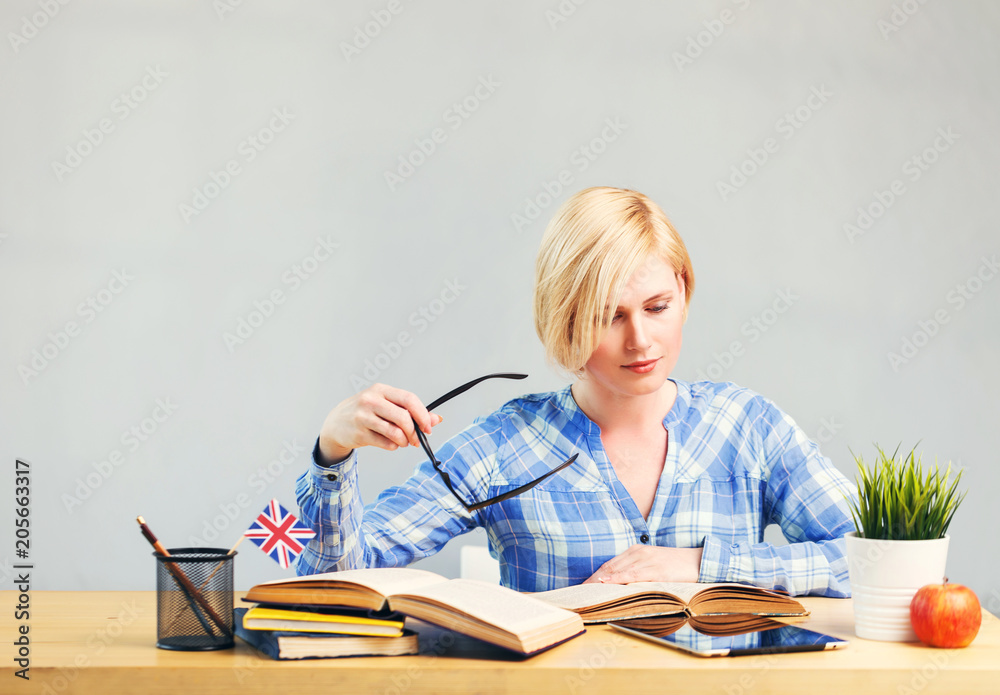 Smart female student, blonde woman holds eyeglasses in hand, studying English language on table with books, successful learning concept Smart female student, blonde woman holds eyeglasses in hand, studying English language on table with books, successful learning concept