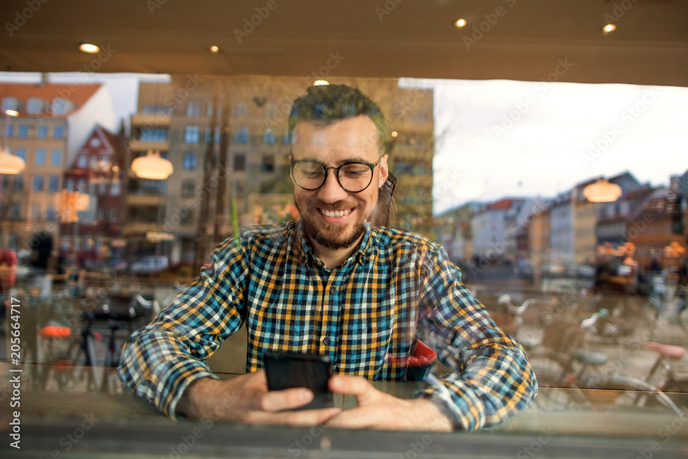 Obraz premium fashion guy with glasses and checkered shirt sitting in a cafe working in the phone