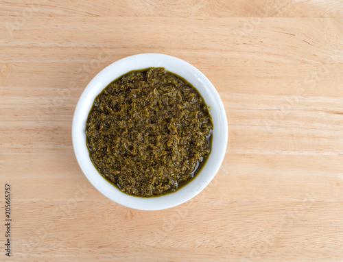 Top view of a bowl of chopped parsley in canola oil on a wood table.