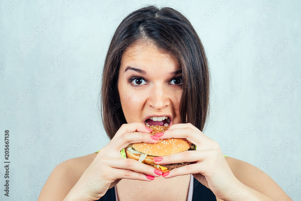 young and attractive woman in black T-shirt and measuring tape eating a high-calorie burger. concept of harmful fast food and diet