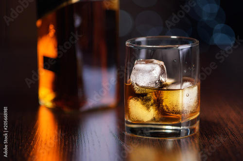 a glass of whiskey on the rocks and a bottle on the table.