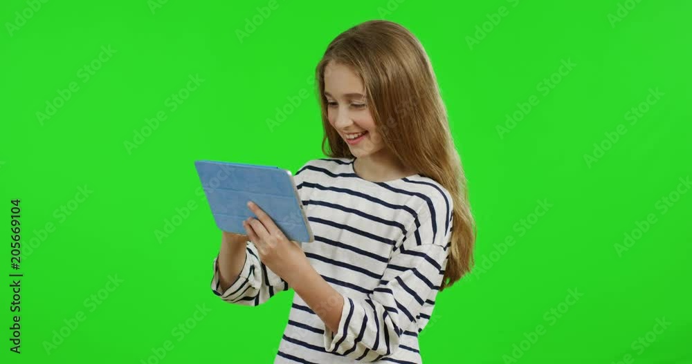 Pretty teen girl with long hair standing on the green screen background and scrolling on the tablet computer screen. Chroma key Pretty teen girl with long hair standing on the green screen background and scrolling on the tablet computer screen. Chroma key