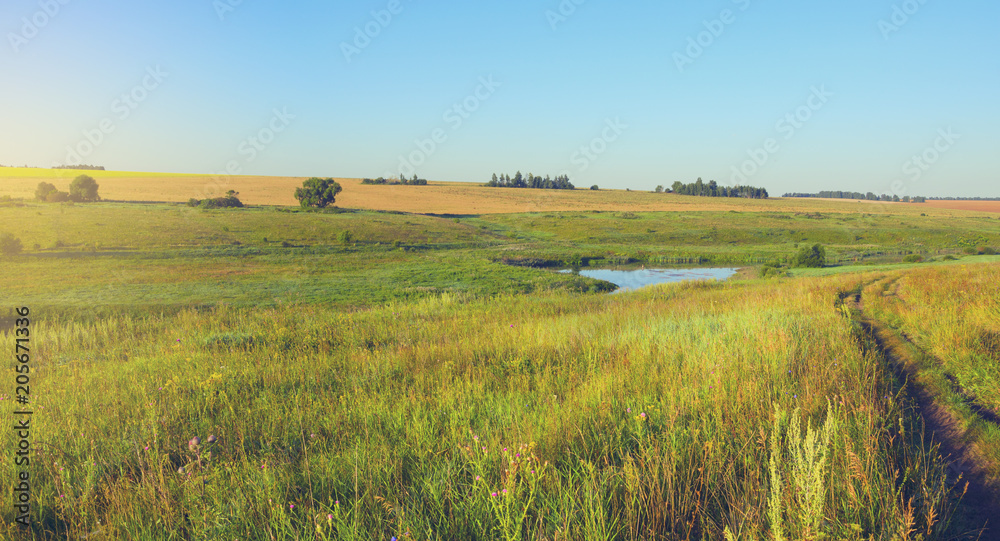 Sunny summer landscape with river.Green hills,fields and meadows on a background cloudless clear blue sky.