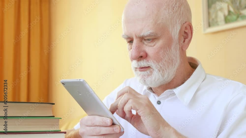 Senior man using online application for learning foreign languages on smartphone. Male student doing in-app training. Active modern life after retirement. Concept of education among elderly people Senior man using online application for learning foreign languages on smartphone. Male student doing in-app training. Active modern life after retirement. Concept of education among elderly people