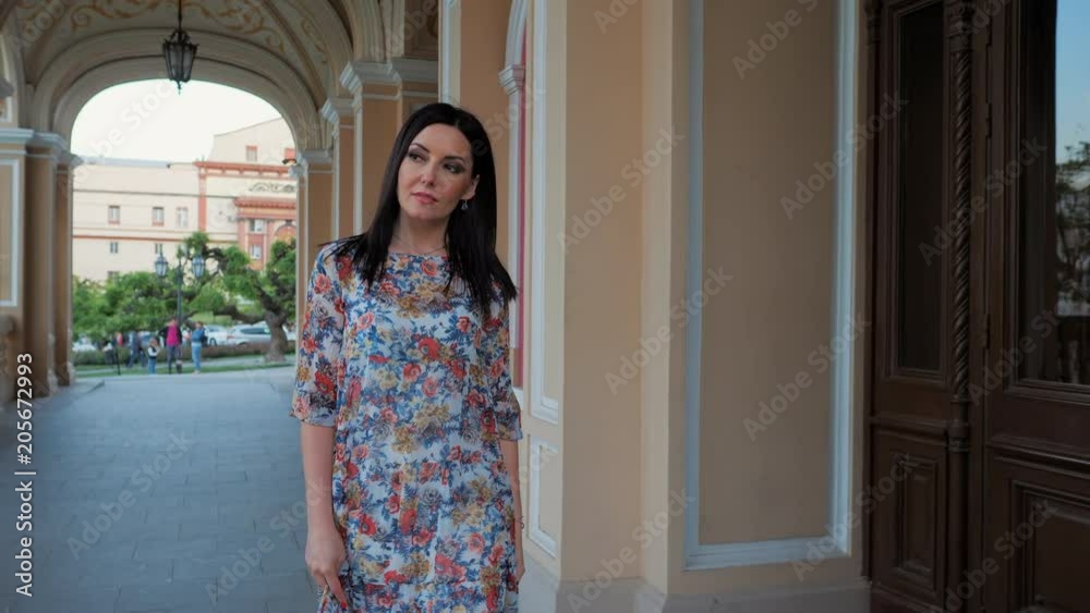 Portrait of adult beautiful mature woman walking on city and architecture background, Lady in silk dress with charming makeup and black hair smiling to camera. Portrait of adult beautiful mature woman walking on city and architecture background, Lady in silk dress with charming makeup and black hair smiling to camera.
