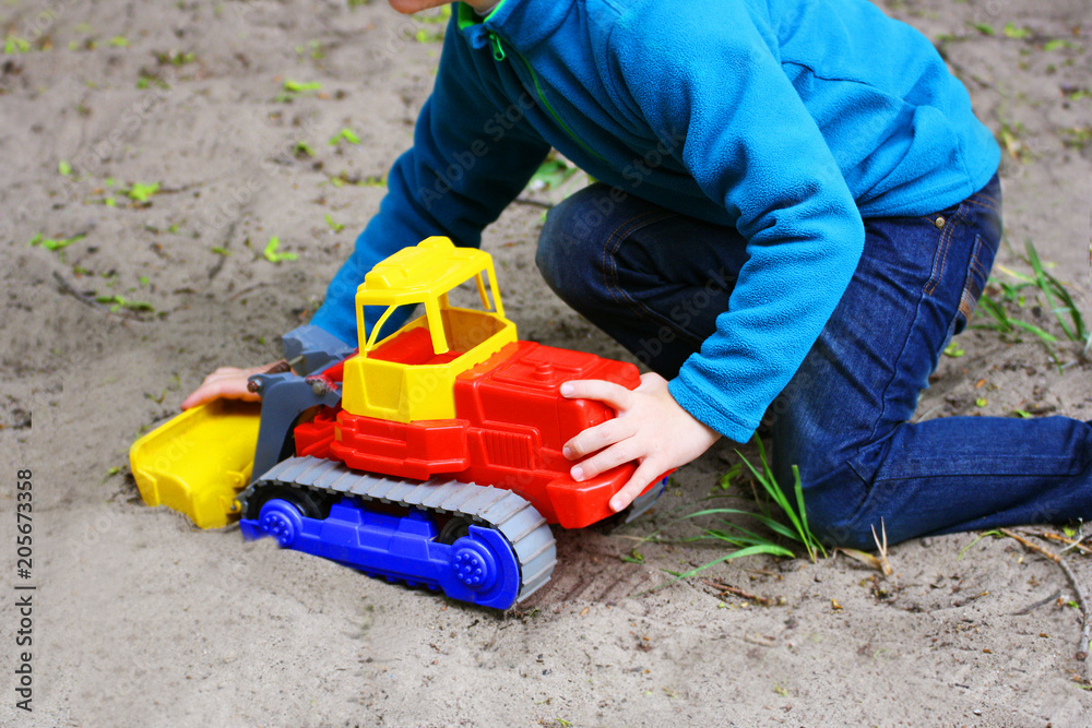 A child playing on the sand with a toy car.
