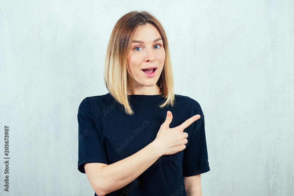 Fototapeta premium portrait of a young and beautiful blonde woman is pointing a finger in a black T-shirt.