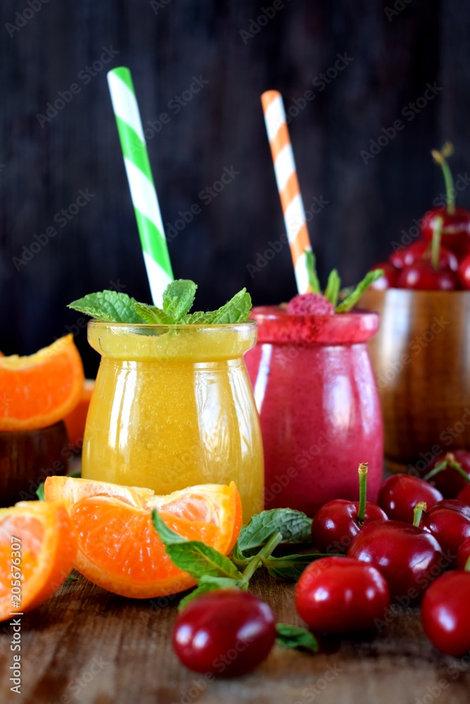 Yellow and red smoothies in glass jars surrounded by mandarins and cherries Yellow and red smoothies in glass jars surrounded by mandarins and cherries