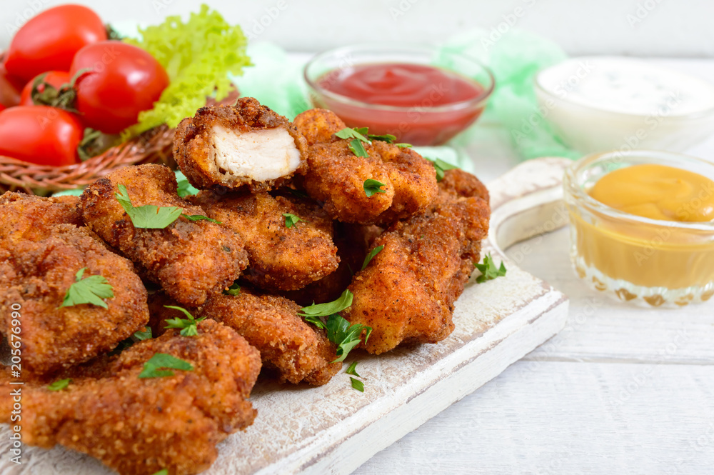Chicken nuggets. Pieces of deep-fried crispy meat, on paper with different sauces on a white wooden table. Traditional snack.