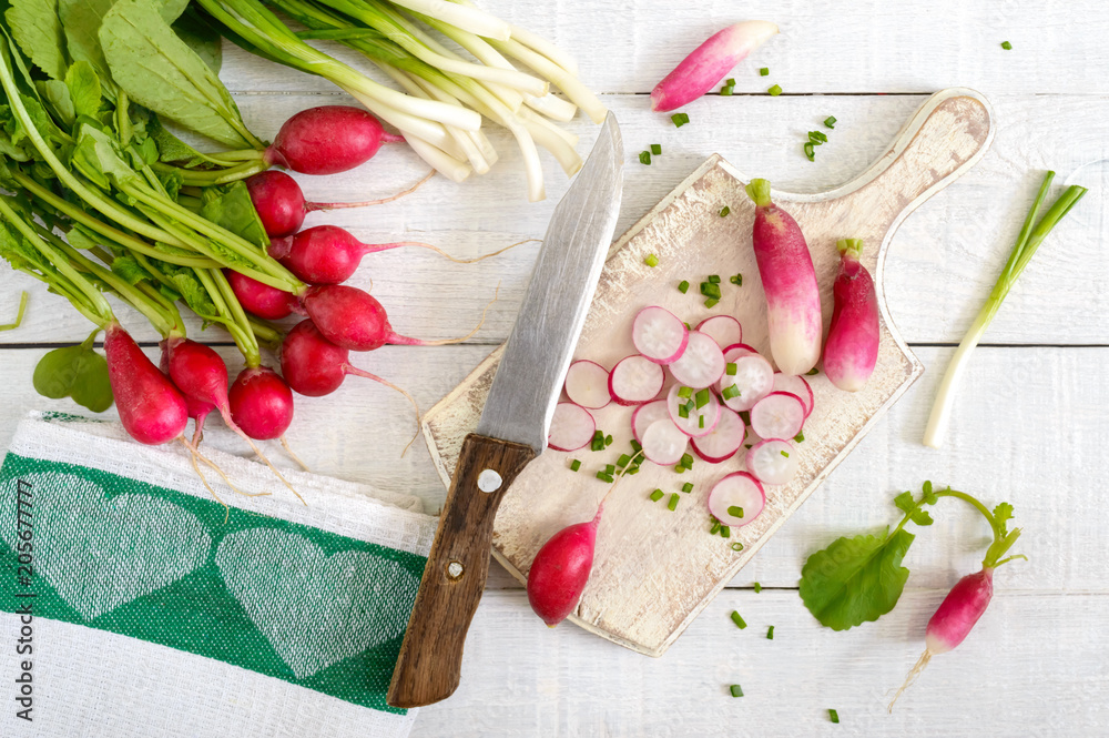Sliced fresh red radishes and green young onions on white wooden background. Healthy diet with radish. Ingredients for a light spring vegetable salad. The top view. Sliced fresh red radishes and green young onions on white wooden background. Healthy diet with radish. Ingredients for a light spring vegetable salad. The top view.