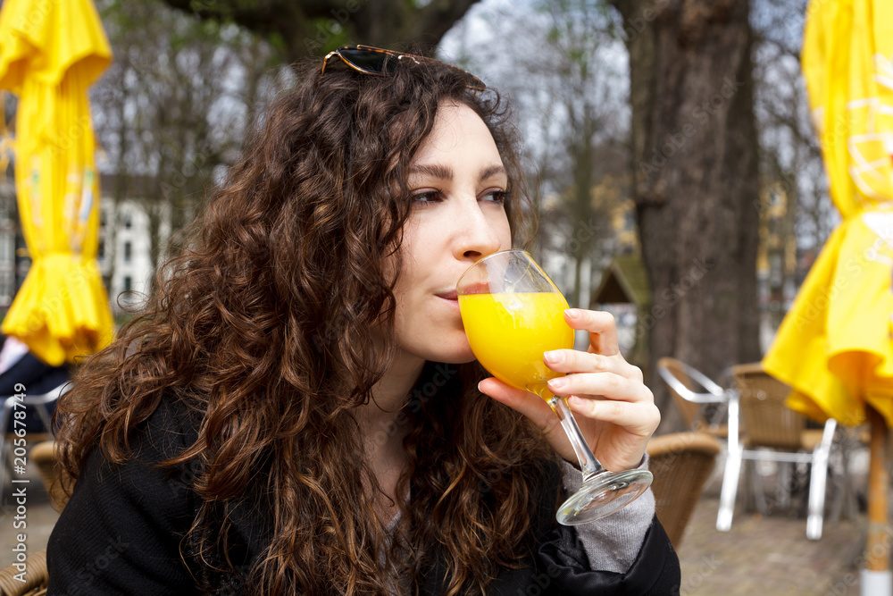 drink fresh juice orange yellow girl coat curly hair smile street Netherland Hague sun spring brunette hand holding glass