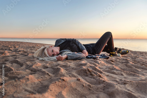 gloomy grim emotionally suffering girl woman lies spinning in the sand on the beach at sunset photo