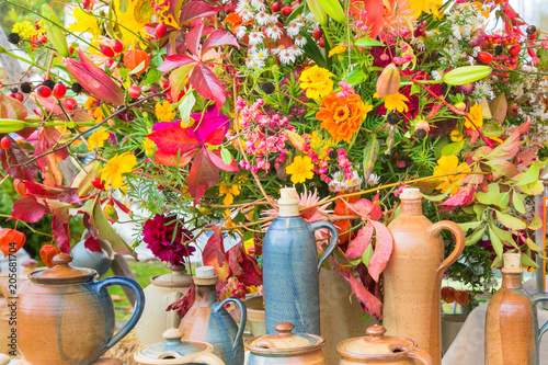 Stilleben mit buntem Strauss von Herbstblumen und passenden Töpferwaren im Vordergrund. Eine schöne stimmung.