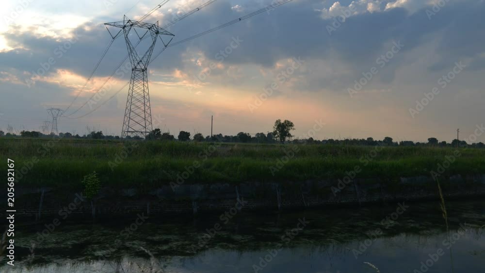 Time lapse of moving water and clouds at sunset overlooking the Naviglio Pavese, Italy. The canal links the city of Milan and Pavia. Tall lattice towers carrying high voltage electricity. Time lapse of moving water and clouds at sunset overlooking the Naviglio Pavese, Italy. The canal links the city of Milan and Pavia. Tall lattice towers carrying high voltage electricity.