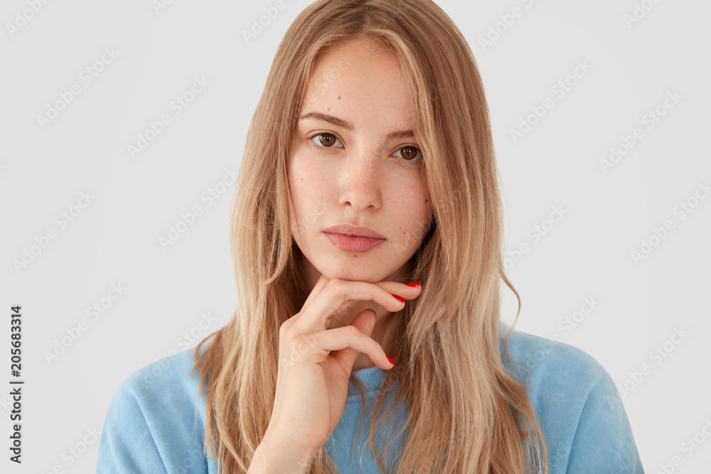 Portrait of lovely young female with serious expression, holds chin, looks confidently at camera, poses against white background, thinks about something. Pretty woman designer has new idea for project Portrait of lovely young female with serious expression, holds chin, looks confidently at camera, poses against white background, thinks about something. Pretty woman designer has new idea for project